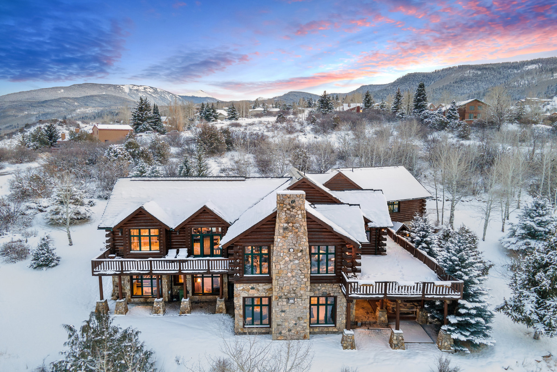 Snow-covered log cabin glowing at sunset in the mountains