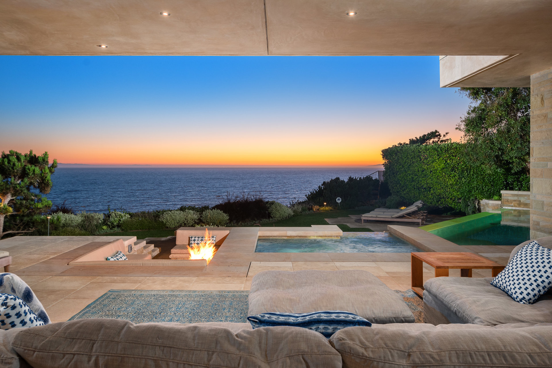 Covered terrace with fire pit and pool above the ocean at sunset