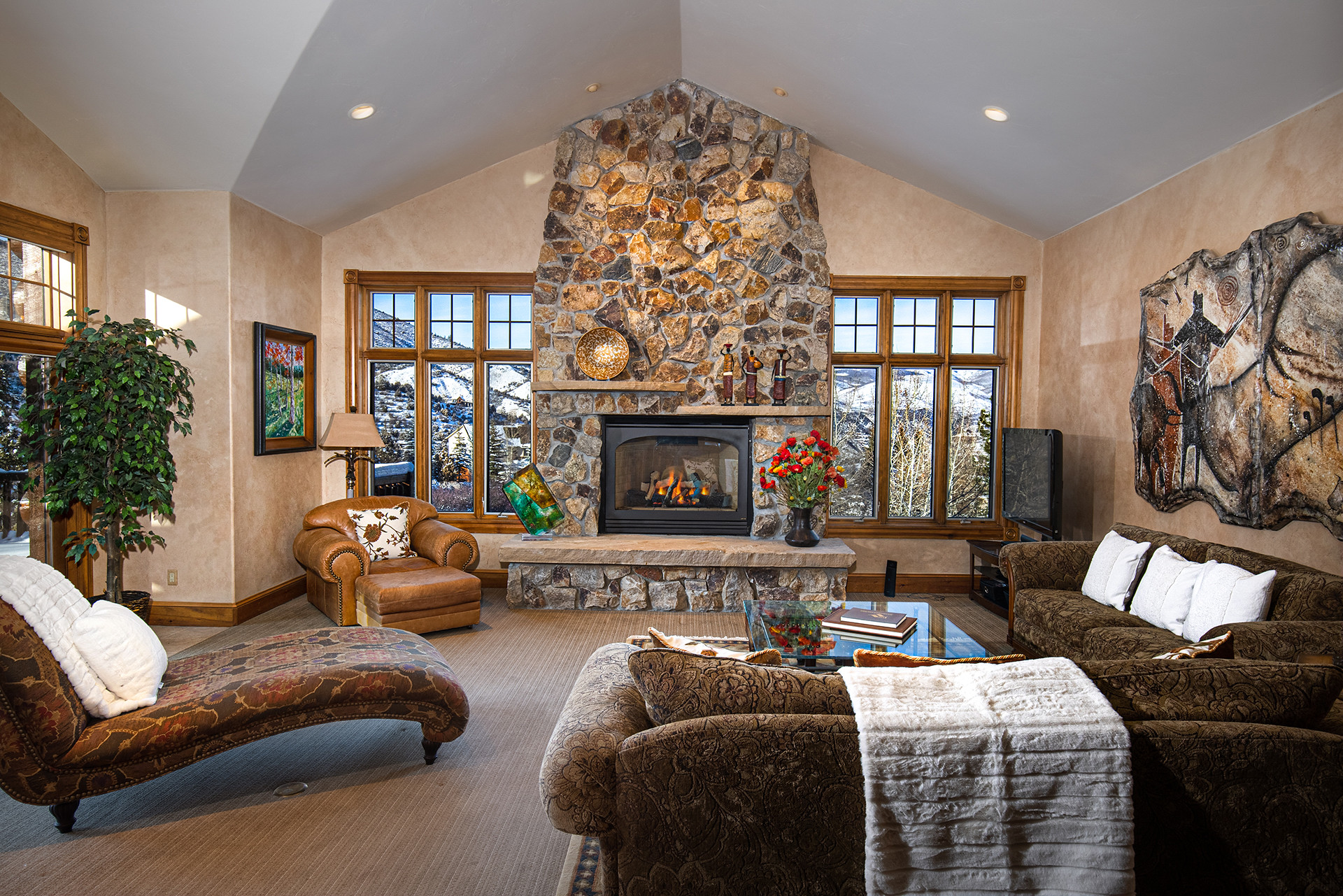 Great room with tall stone fireplace and snowy windows