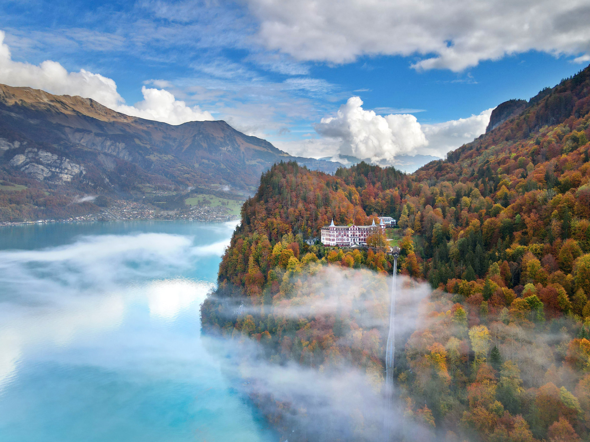 Aerial view of a grand hotel above a turquoise alpine lake