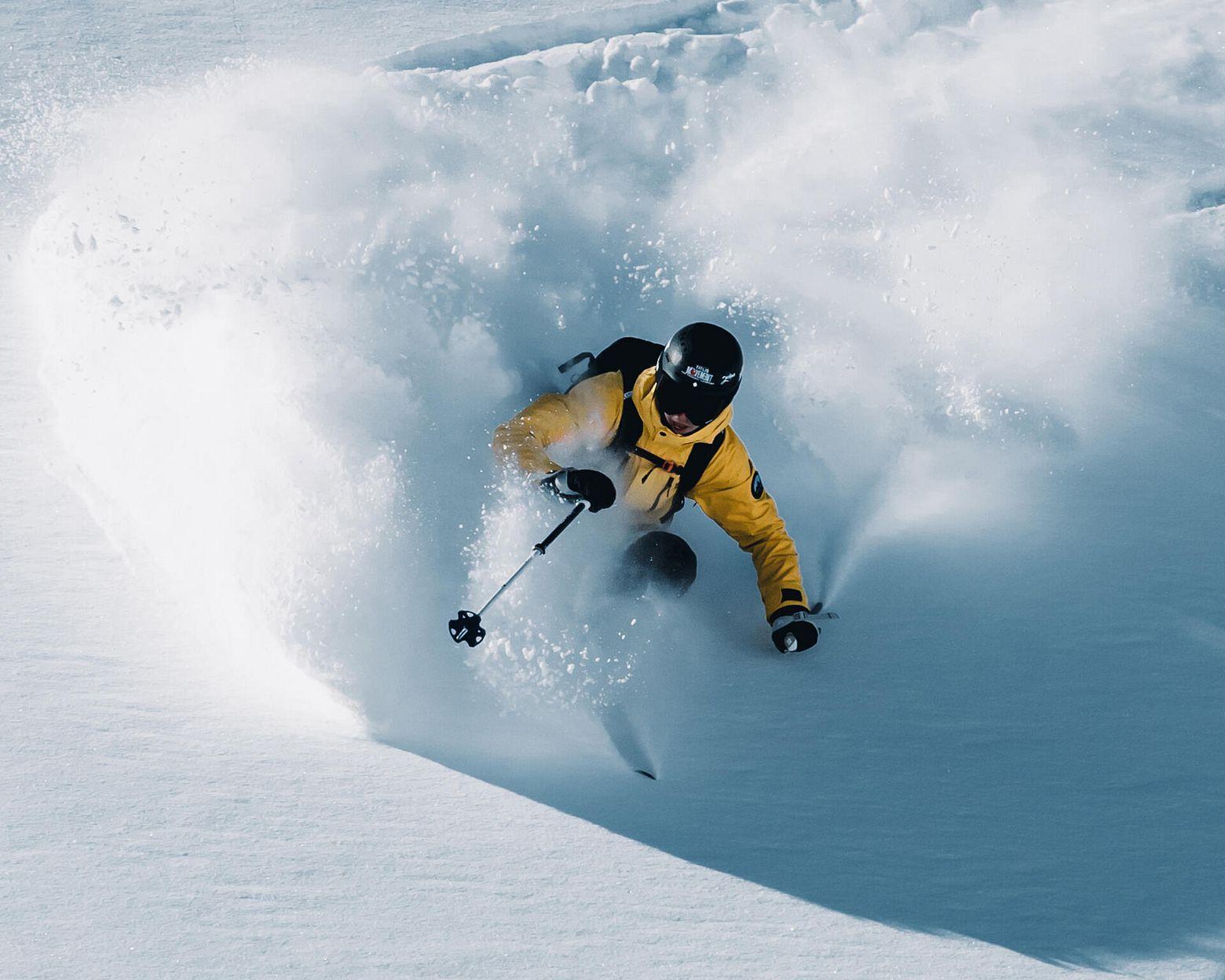 A skier carving through fresh powder in a spray of snow