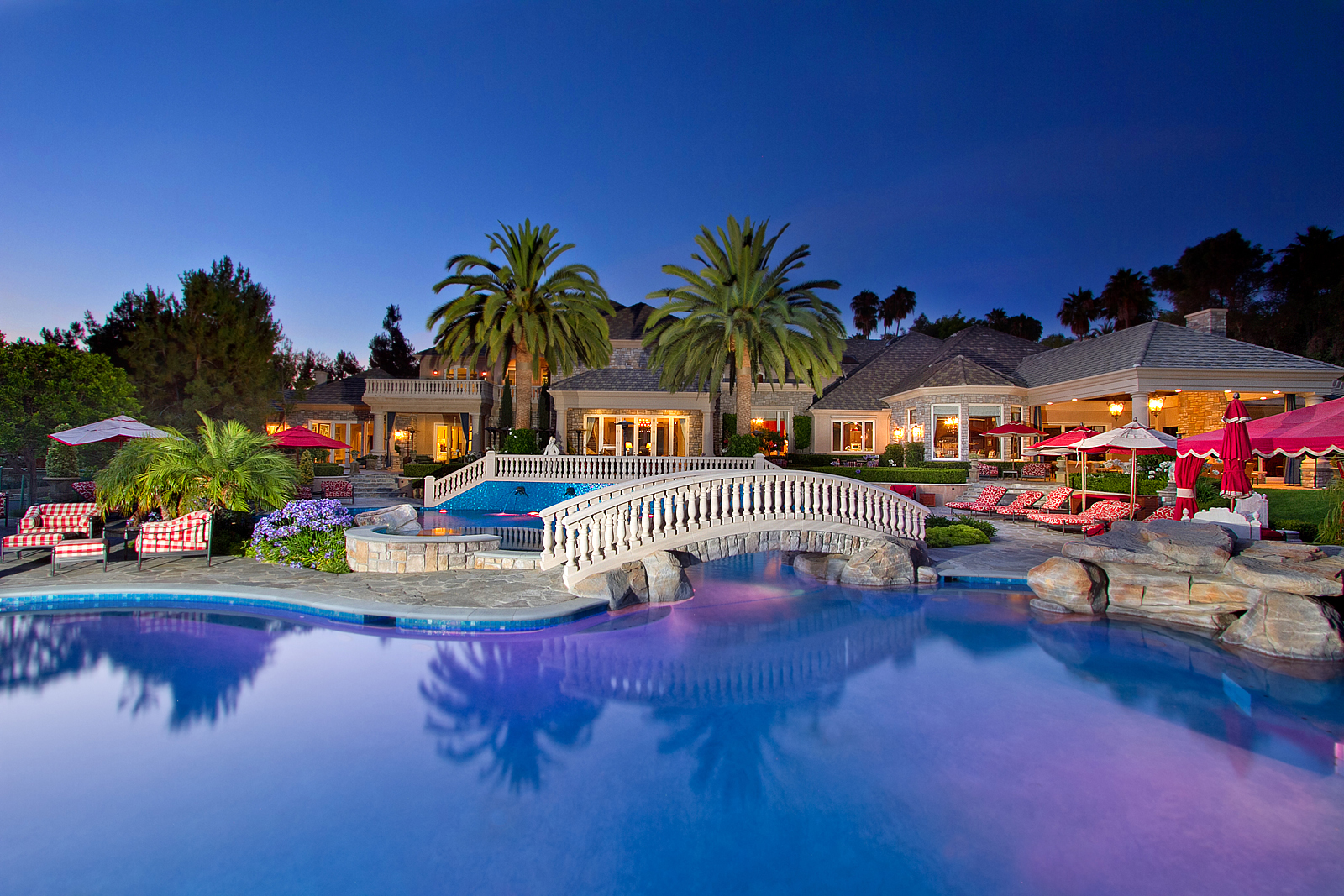 Resort-style pool with stone bridge at dusk