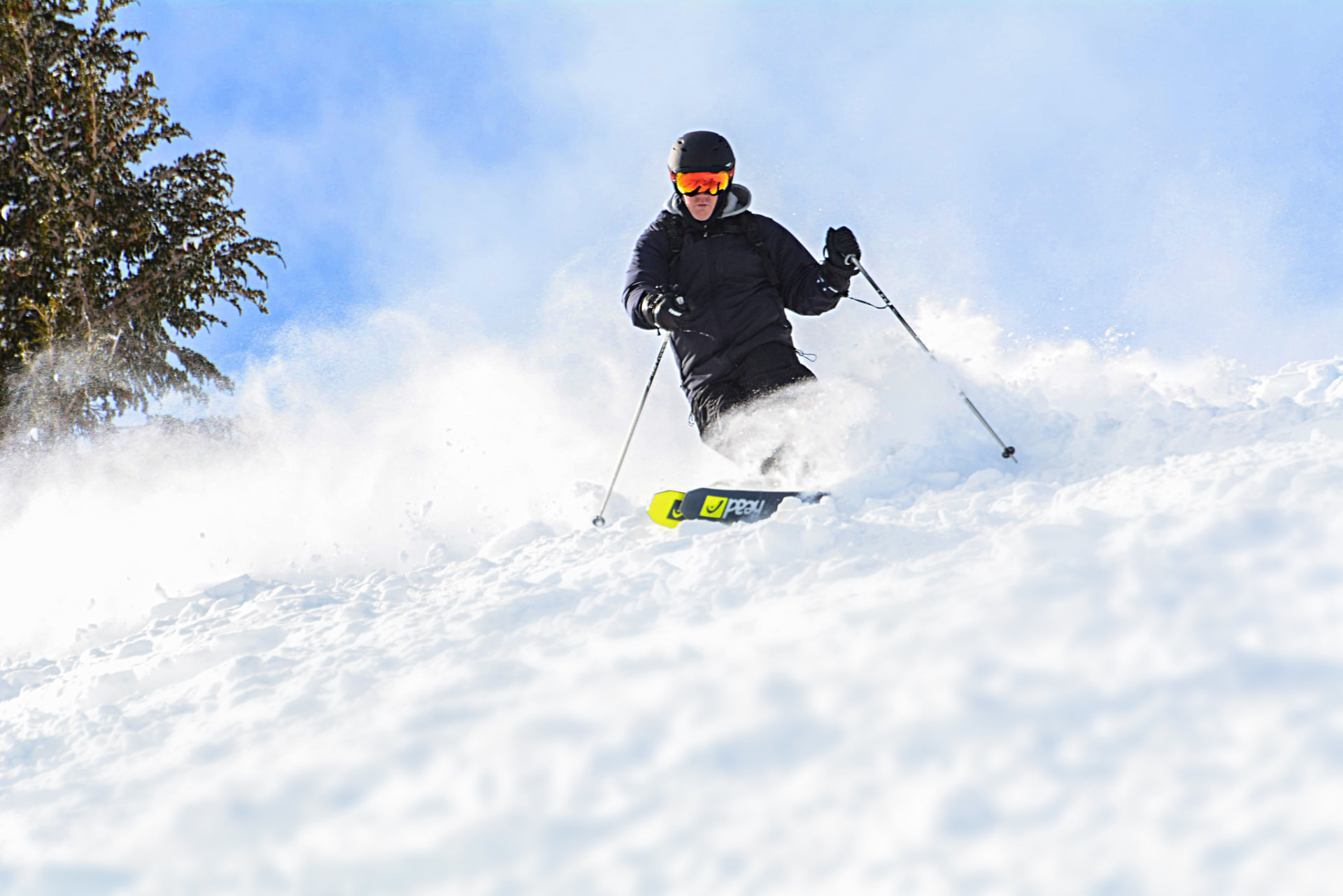 Skier carving through deep powder under a blue sky