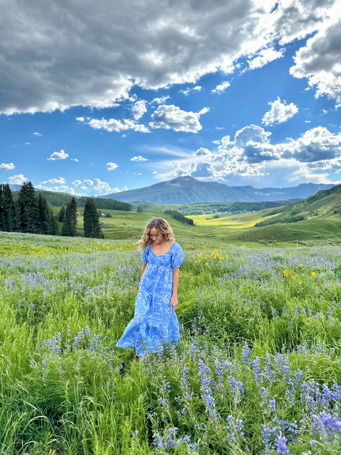 Young woman in a blue dress walking through a wildflower meadow