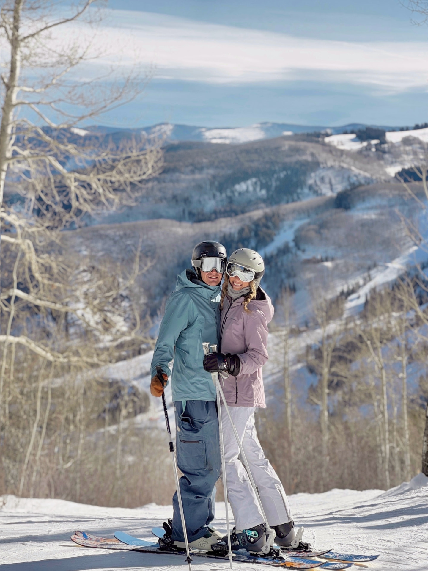 Couple in ski gear posing together on a snowy overlook above the valley